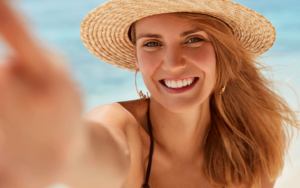 Mulher de chapéu de palha na praia sorrindo e olhando para a câmera 